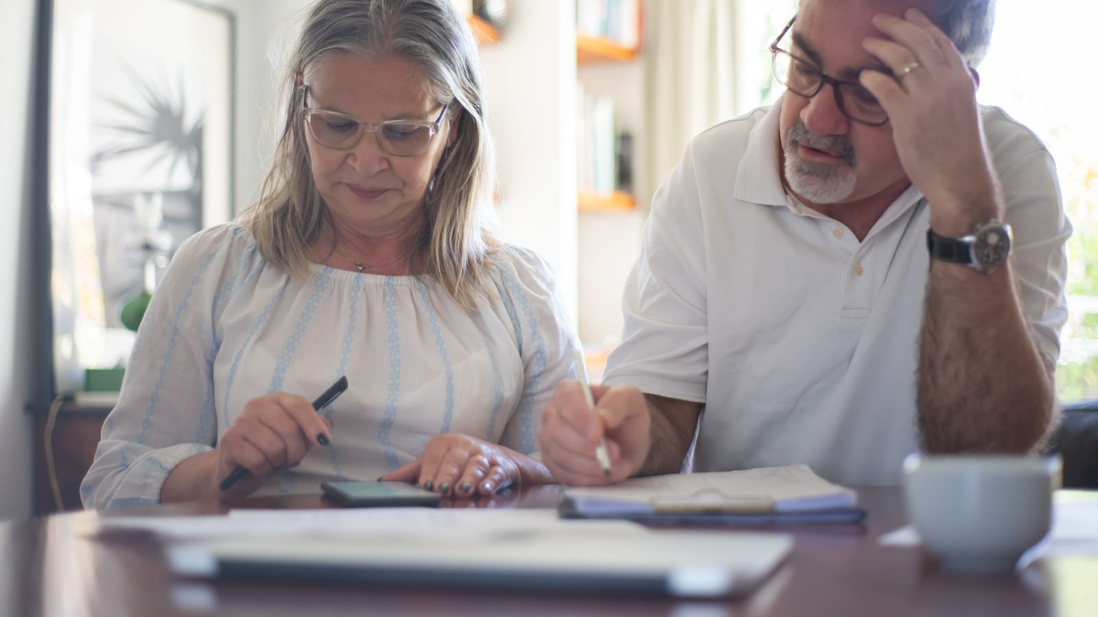Pareja mayor comparando planes de Medicare con documentos y computadora en la mesa de su casa