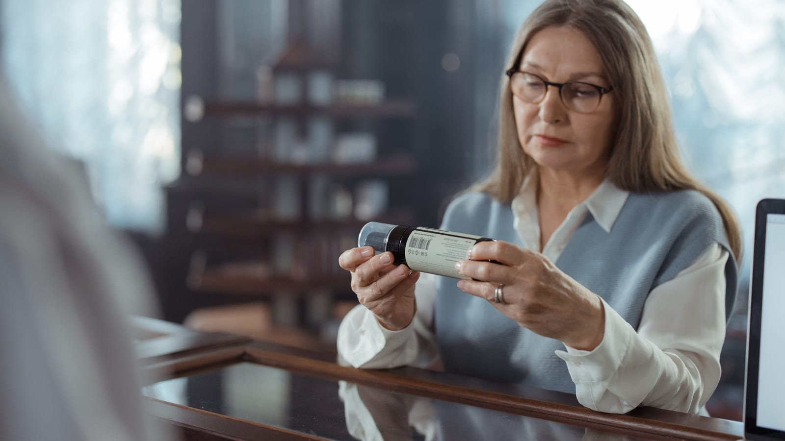 Adulta mayor con lentes revisando un frasco de medicamento en el mostrador de una farmacia